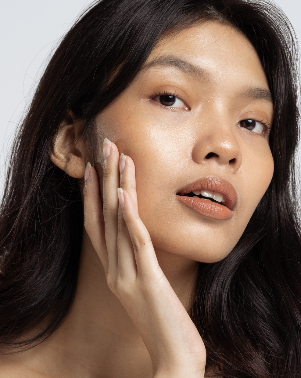 A woman is touching her face with her hand and looking at the camera.