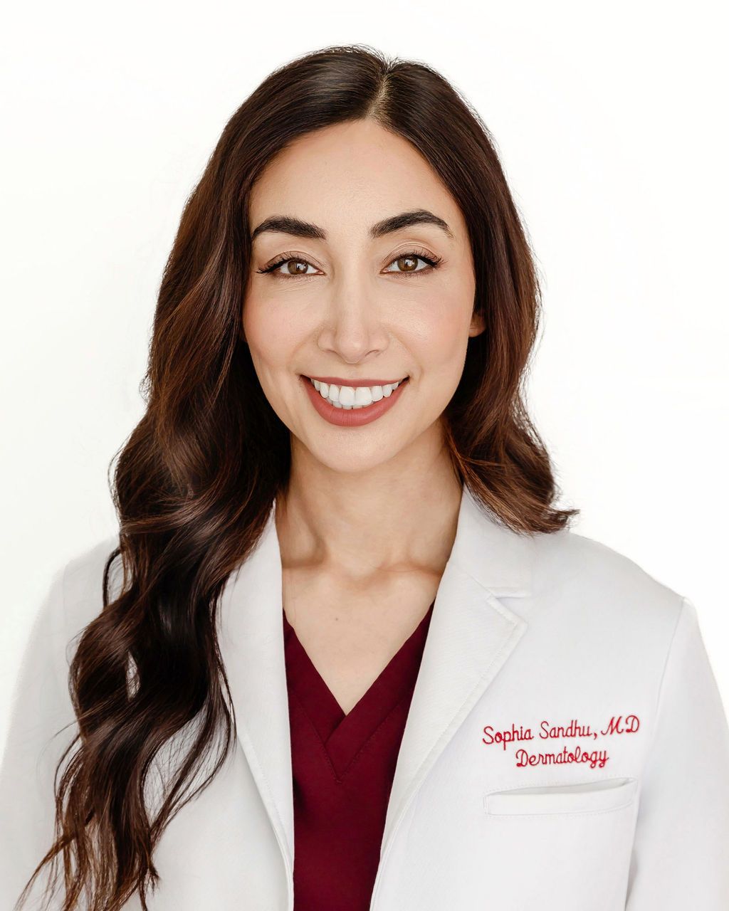 A woman in a white coat and red scrub is smiling for the camera.