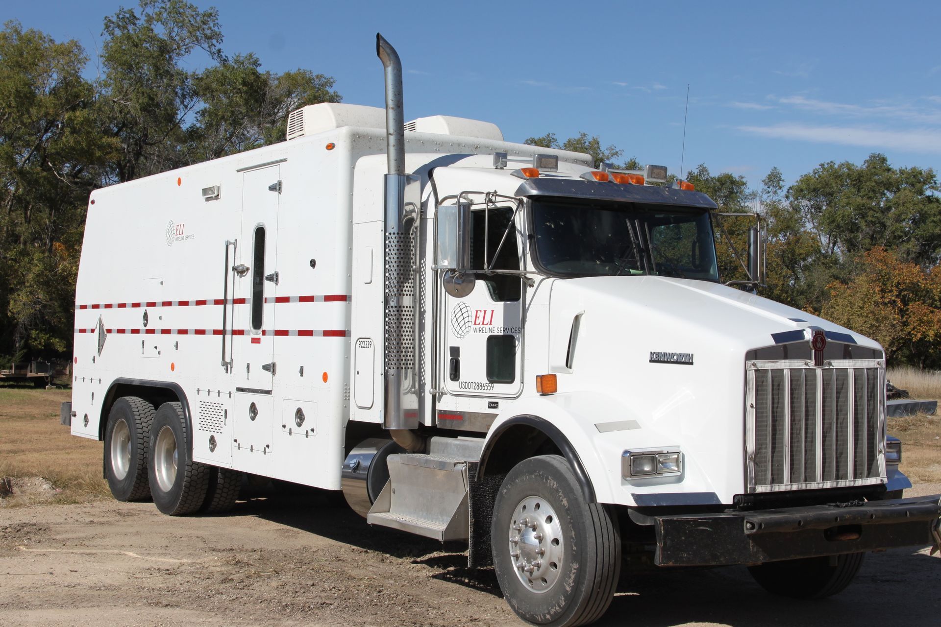 A white truck is parked in a dirt field with trees in the background.