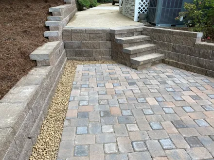 Stone patio with raised retaining walls and steps leading to a paved walkway.
