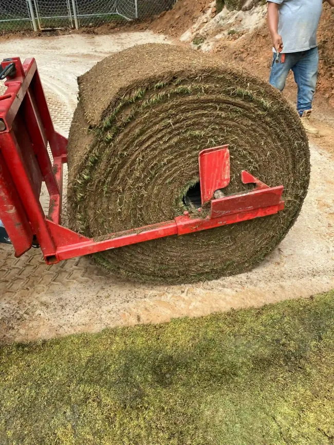 Large rolled hay bale on a red trailer, with a person standing beside it outdoors.