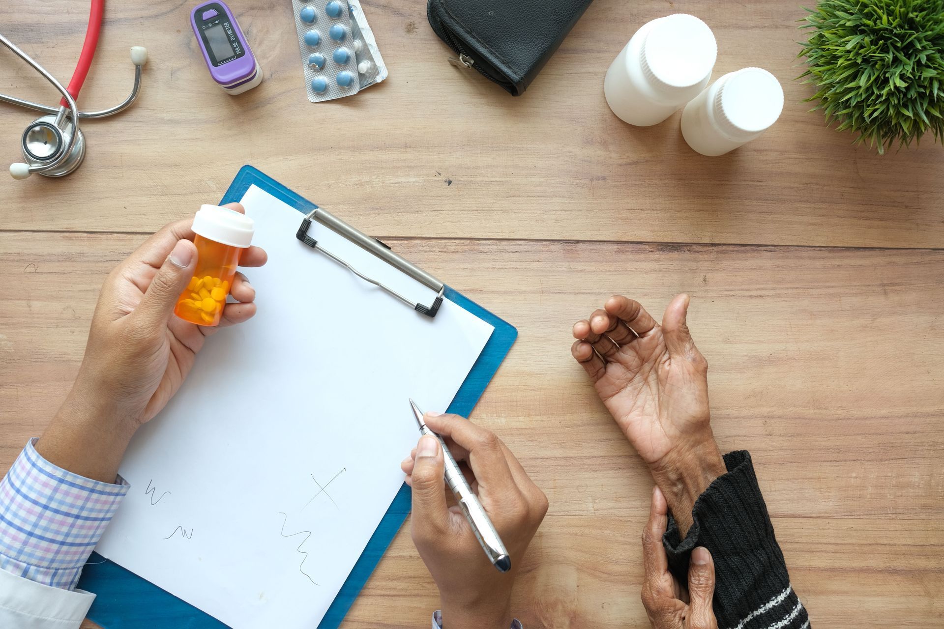 Hands writing on a clipboard at a wooden desk with medicine bottles and pills nearby