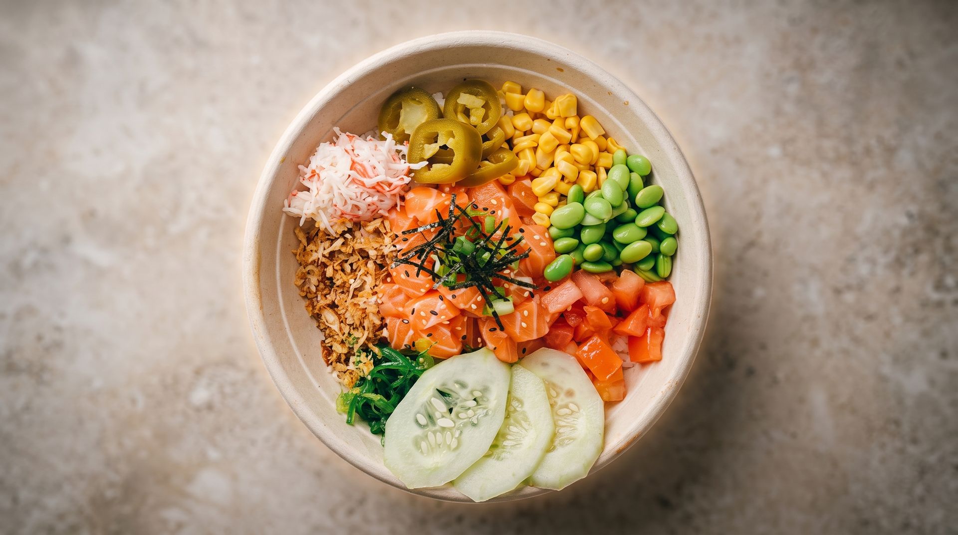 Colorful poke bowl with salmon, rice, avocado, corn, cucumber, and radish on a stone table