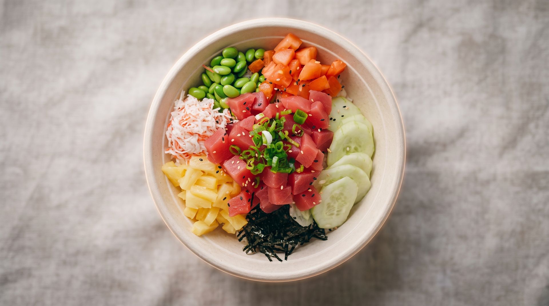 A bowl of colorful poke with rice, salmon, avocado, edamame, cucumber, mango, seaweed, and sesame seeds