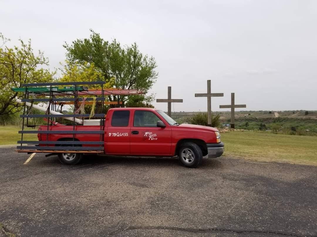 A red truck with a ladder on the back is parked in a parking lot.