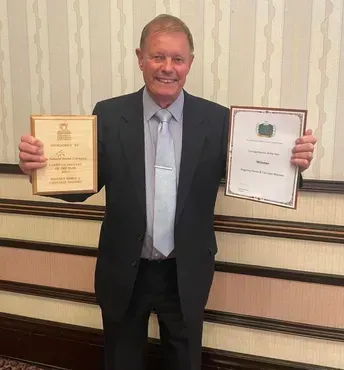 A man in a suit and tie is holding two awards in his hands.