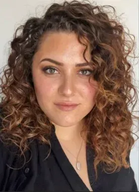 A woman with curly hair is wearing a black shirt and a necklace.