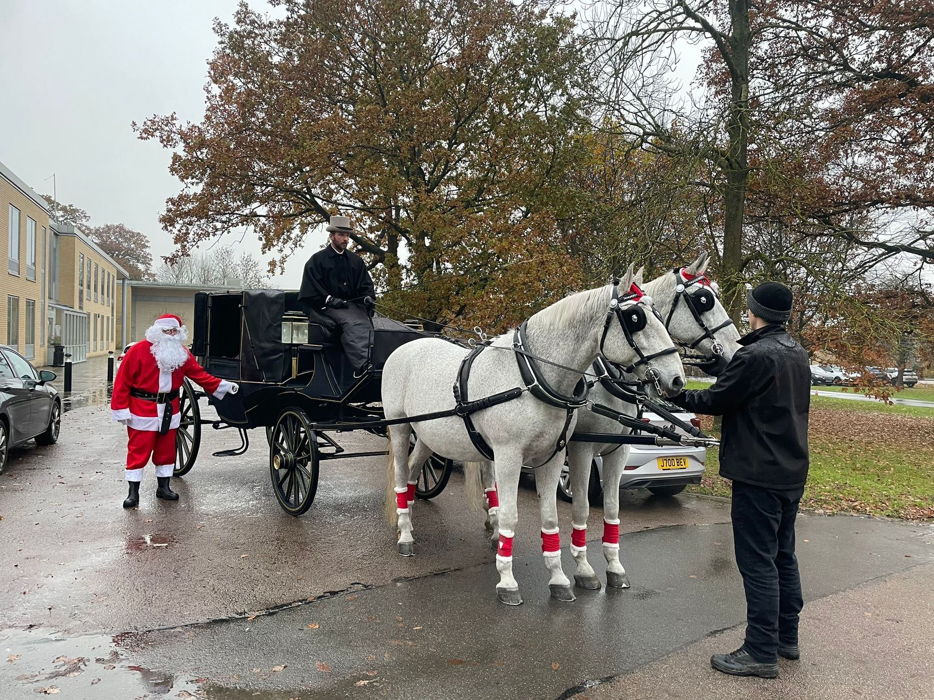 A man dressed as santa claus is standing next to a horse drawn carriage.
