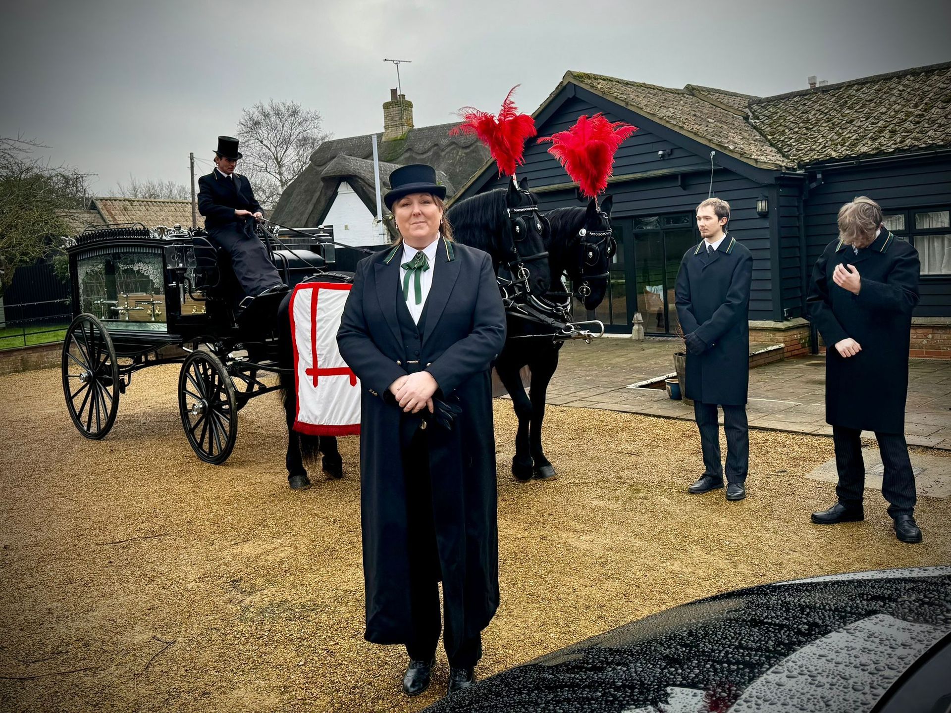 A man in a top hat stands in front of a horse drawn carriage