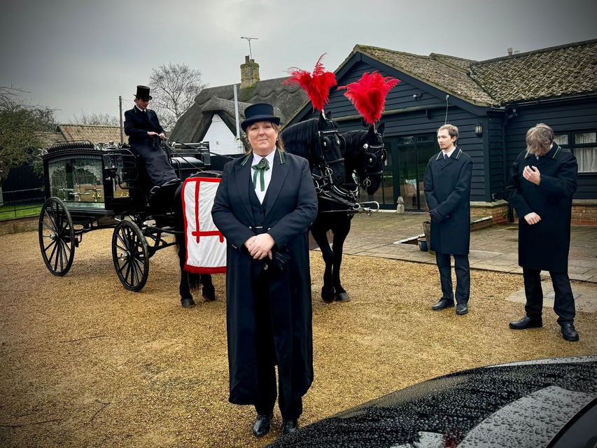 A man in a top hat stands in front of a horse drawn carriage