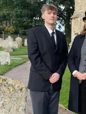 A man in a suit and tie is standing next to a woman in a coat in a cemetery.