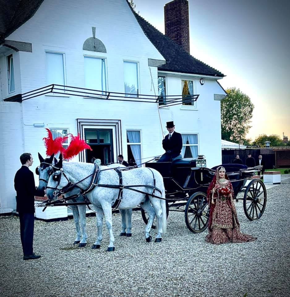 A bride and groom are standing in front of a horse drawn carriage