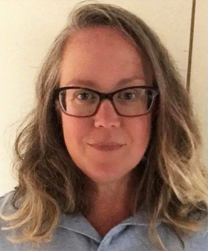 A woman wearing glasses and a blue shirt is smiling for the camera.