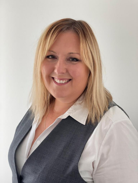A woman wearing a vest and a white shirt smiles for the camera