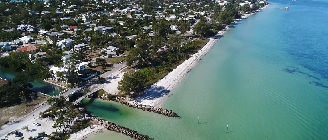 Aerial view of a tropical beach with turquoise water, white sand, and dense trees along the shore