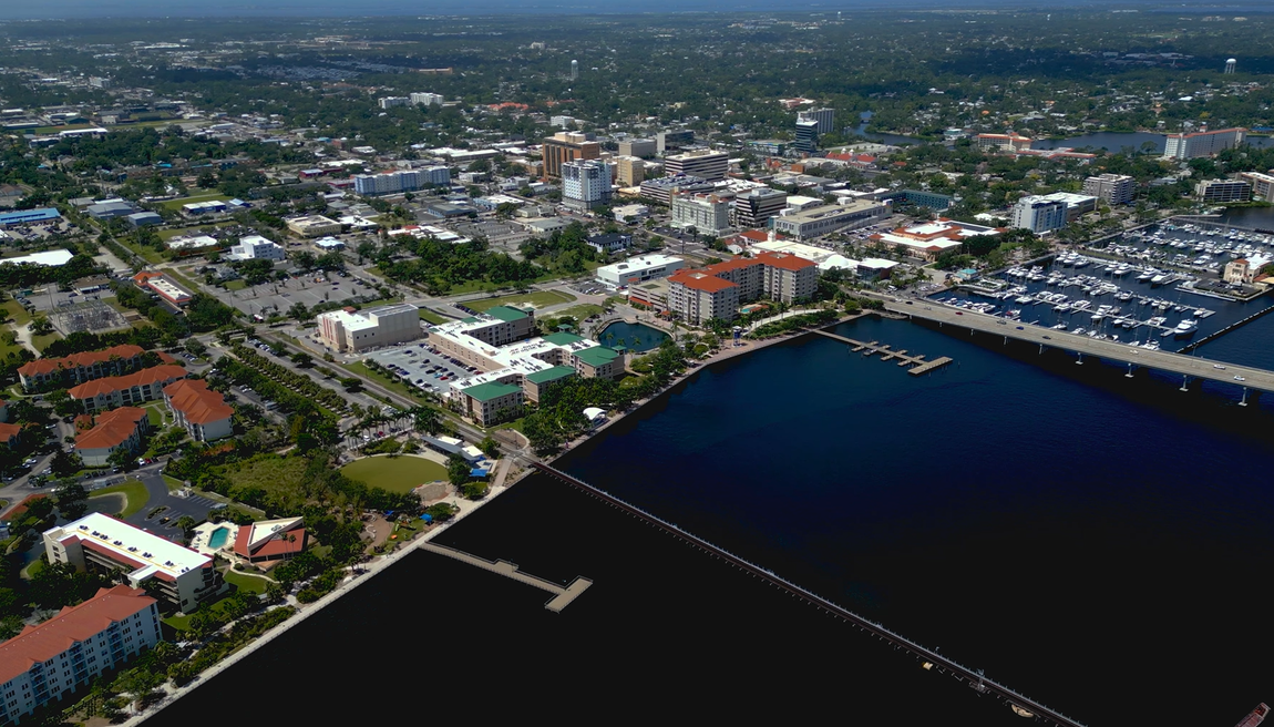 Aerial view of a coastal city with a marina, waterfront buildings, and dense urban neighborhoods.
