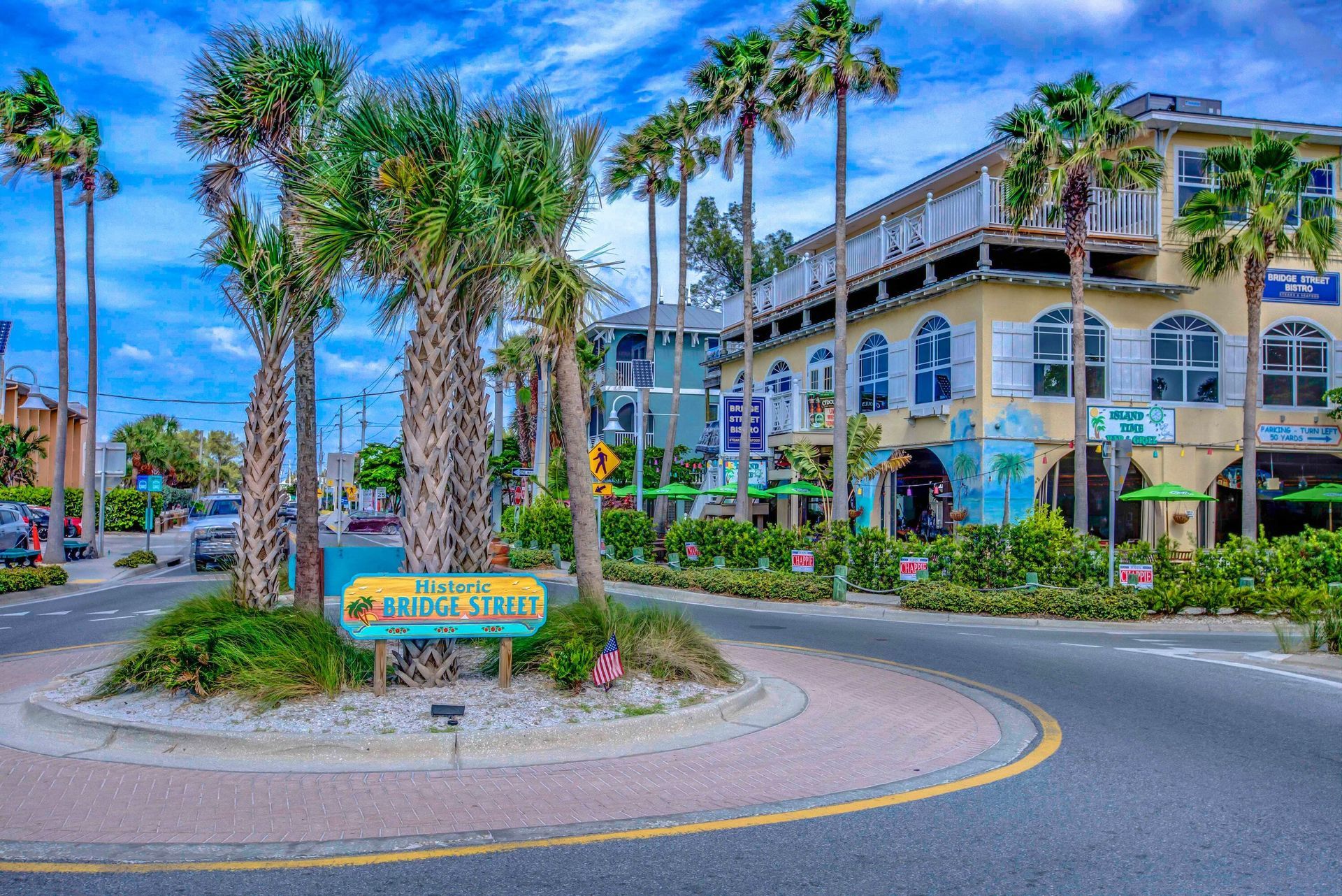 Tropical resort entrance with palm trees, a roundabout, and a building with arched balconies.