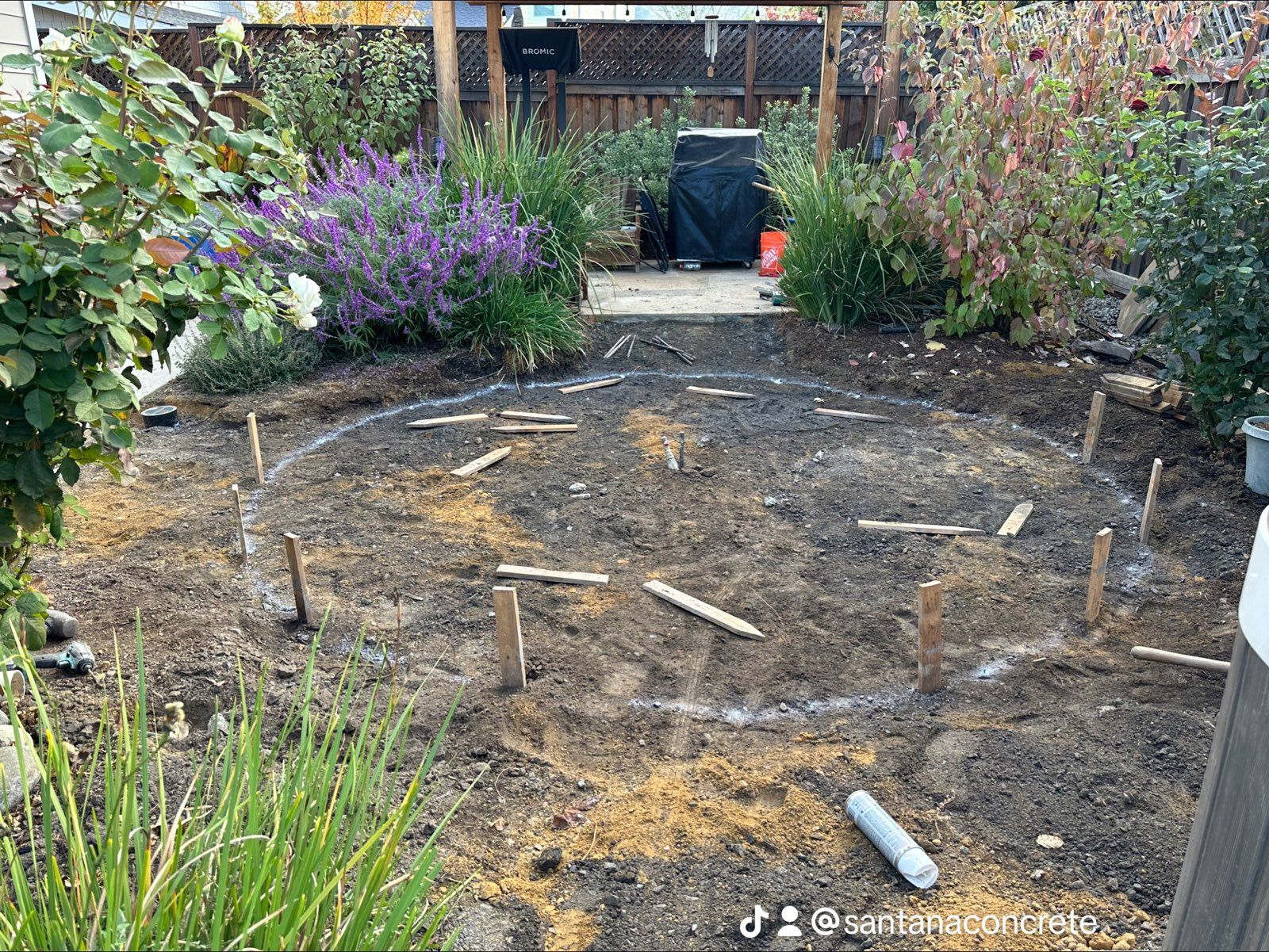 A circle of wooden posts in the dirt in a garden.