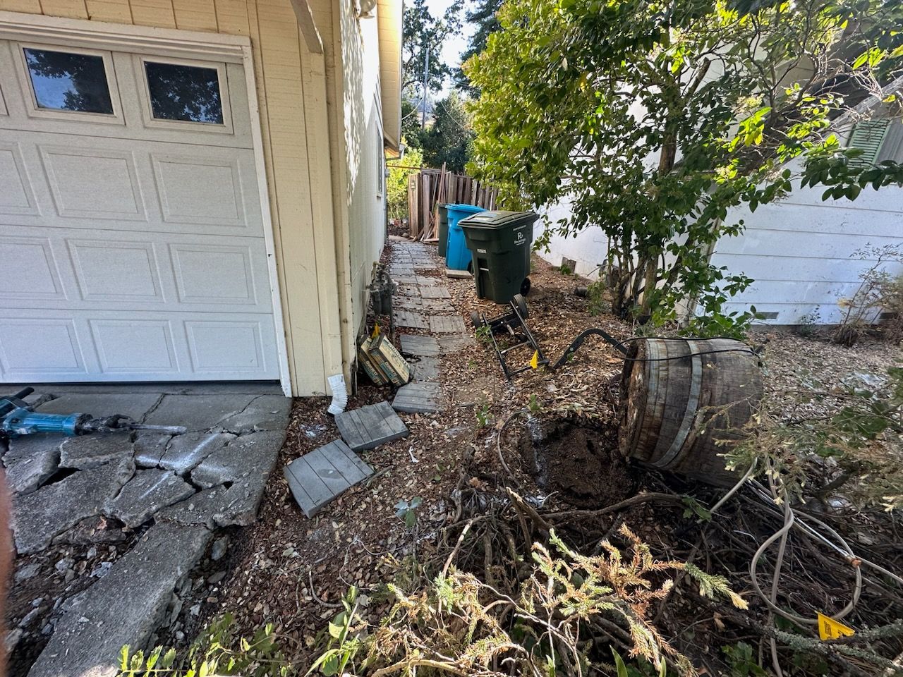There is a barrel in the middle of the yard next to a garage door.