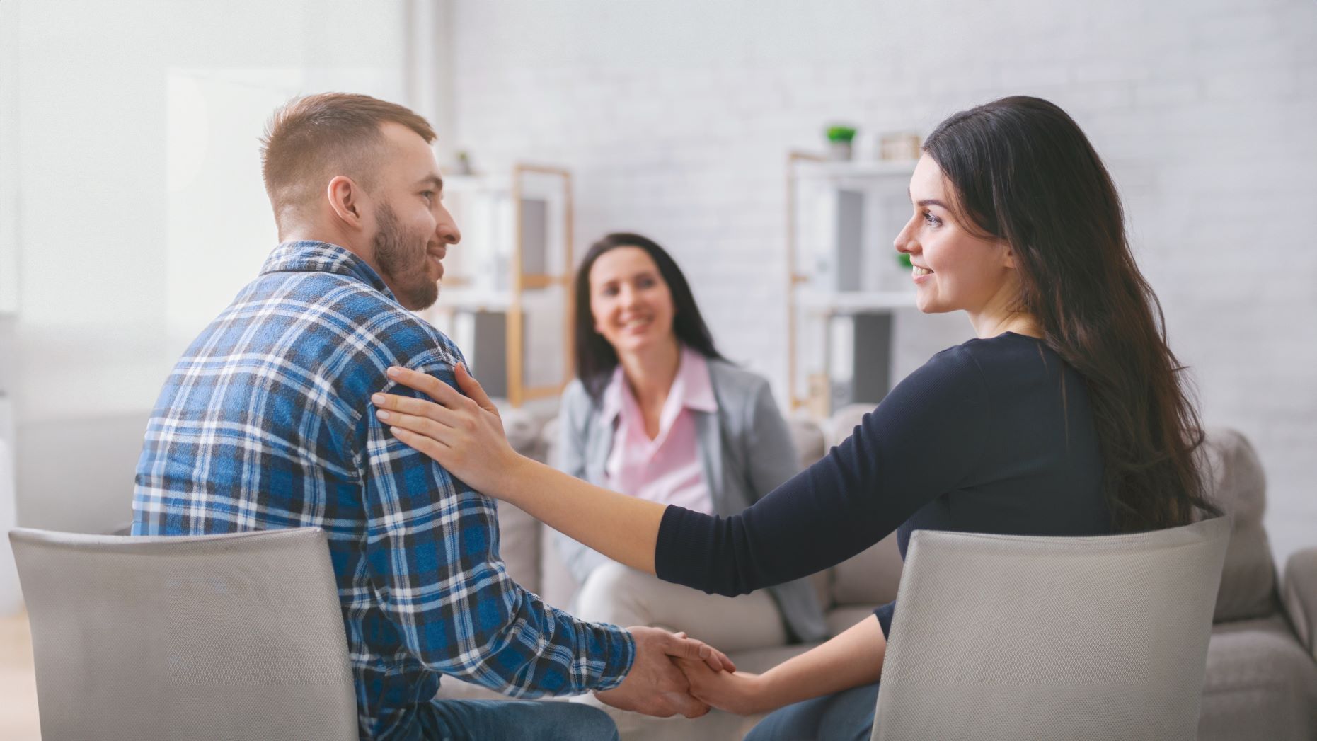 A man and a woman are holding hands while sitting on a couch.