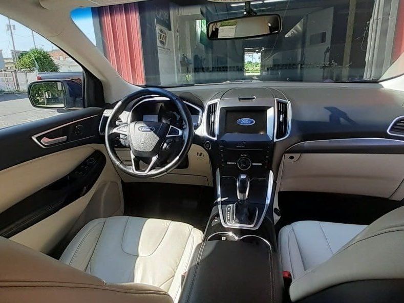 Interior of a beige and black Ford Edge. Shows the dashboard, steering wheel, seats and console.