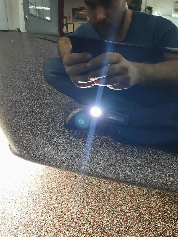 Man using a flashlight to inspect a car's bumper in a garage.