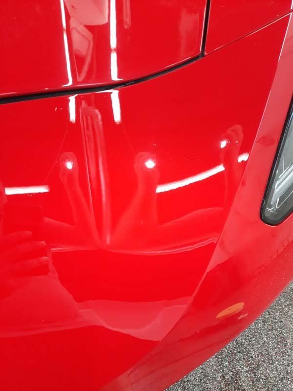 Shiny red car hood reflecting bright lights.