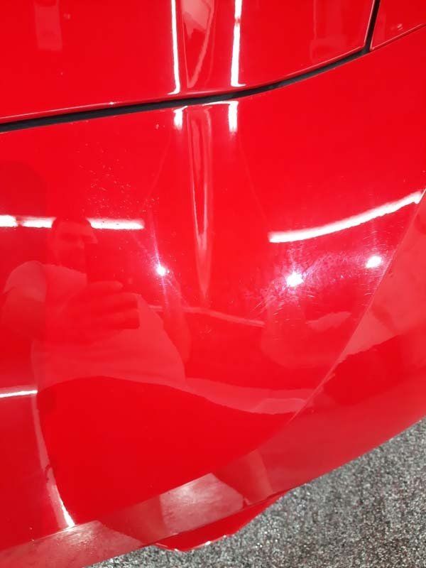 Red car hood with dents and imperfections; reflections of lights.