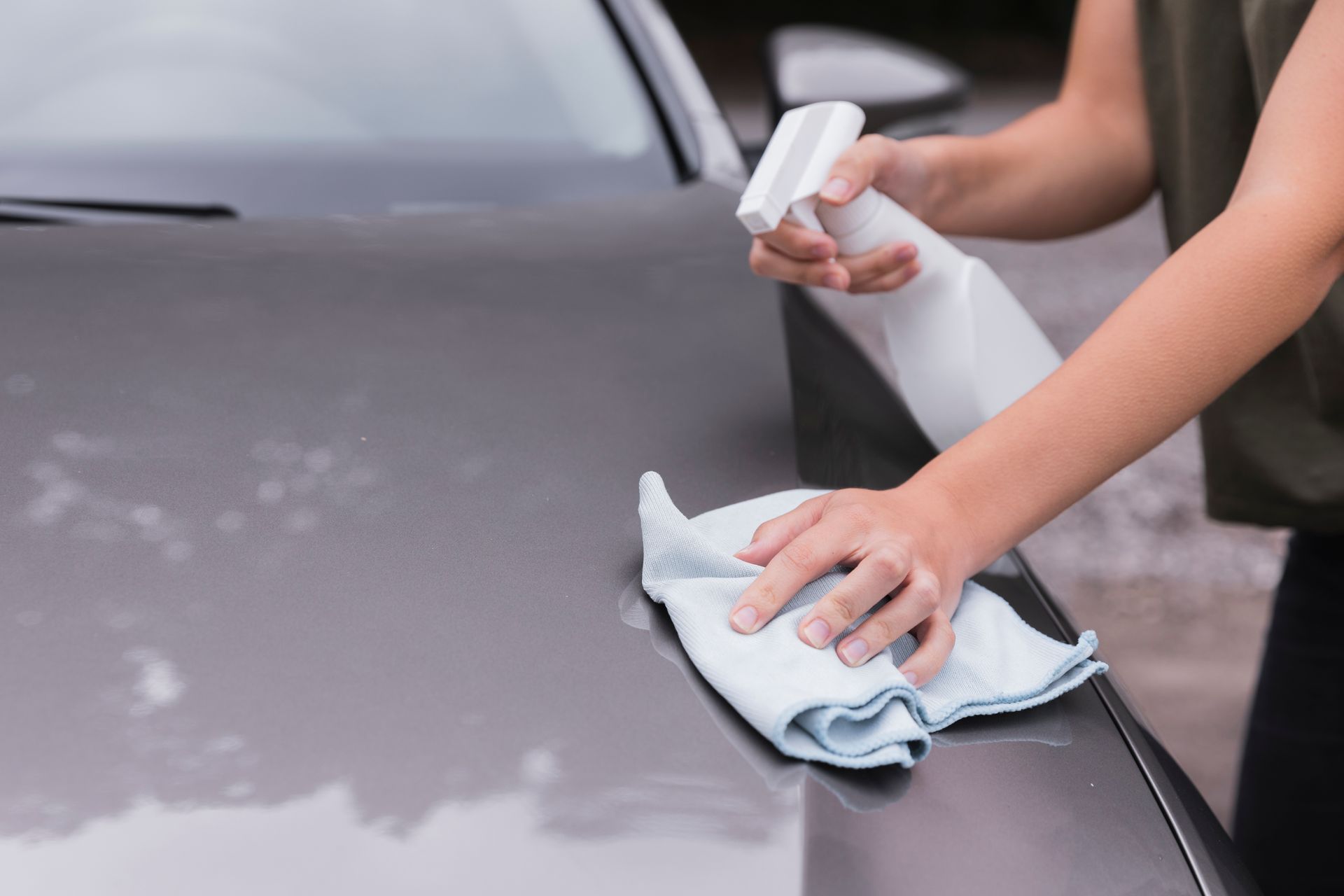 A woman is cleaning a car with a towel and spray bottle.