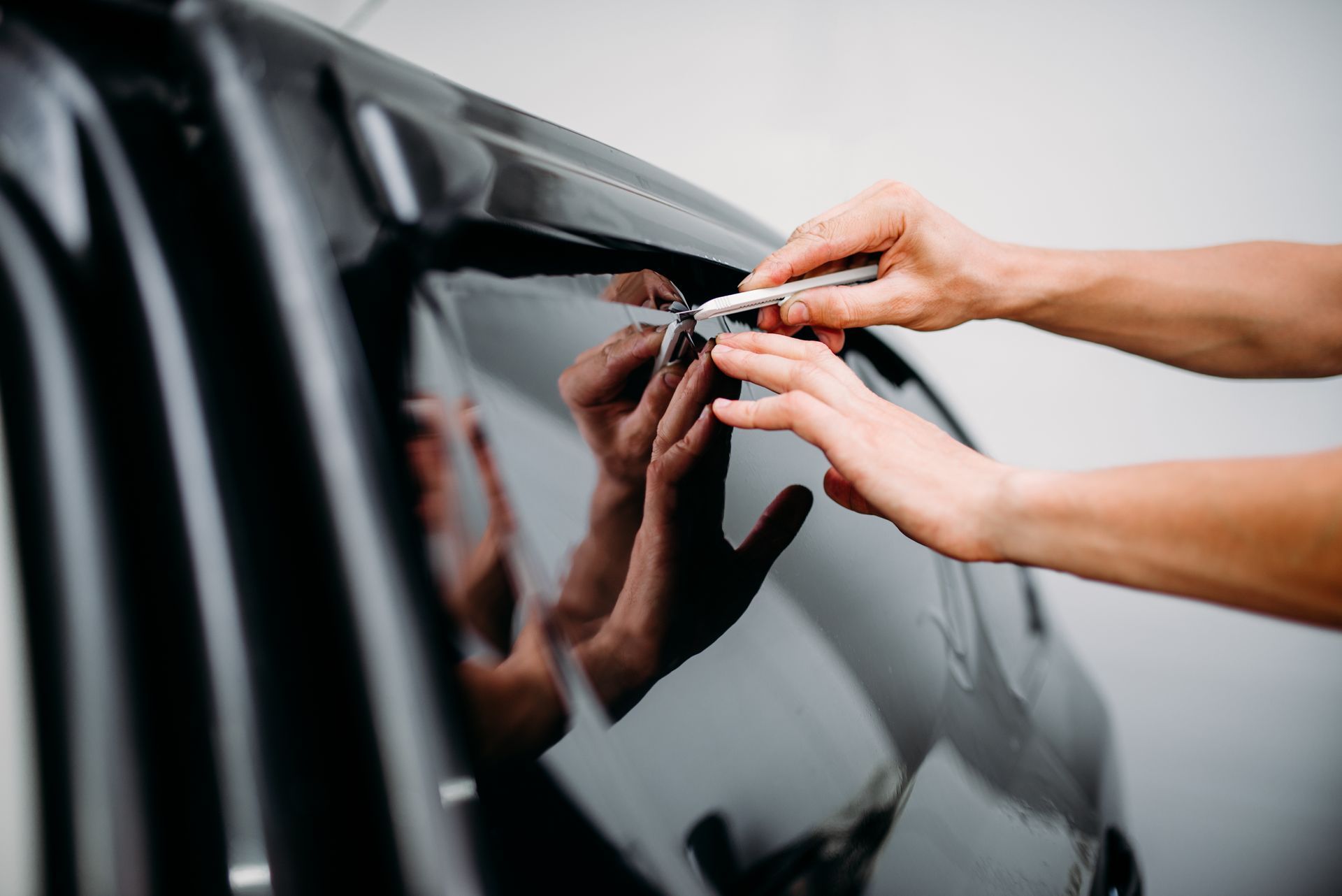 A person is applying tinted window film to a car window.