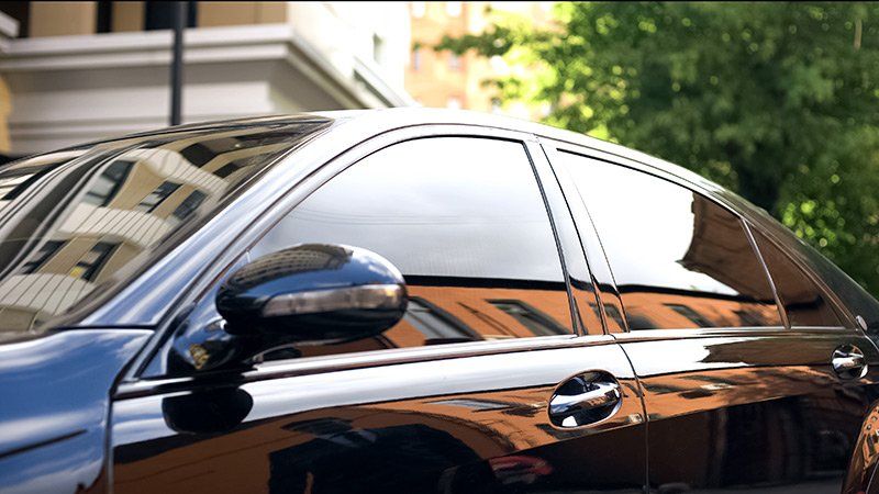 Black car with tinted windows reflecting buildings and greenery.