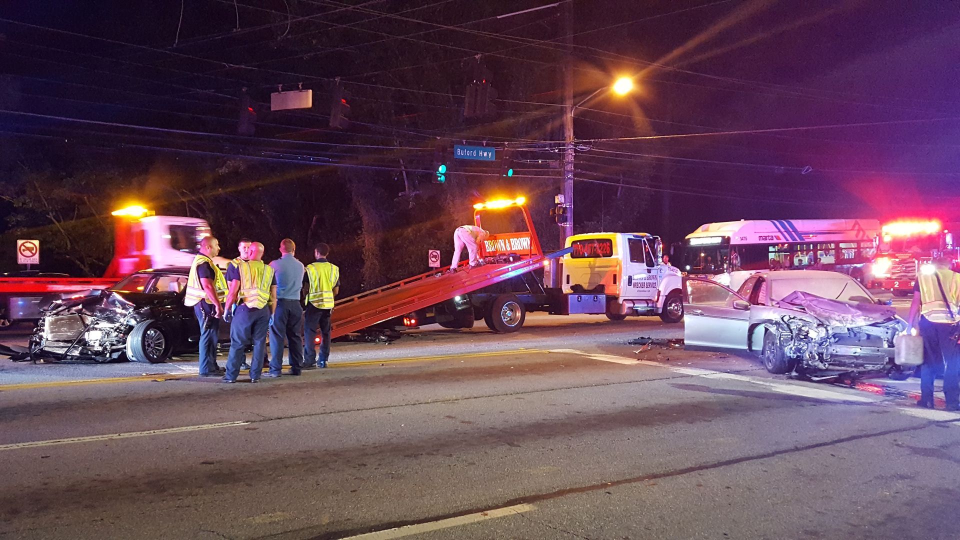 Emergency responders at a nighttime car crash with damaged vehicles and flashing lights on the road