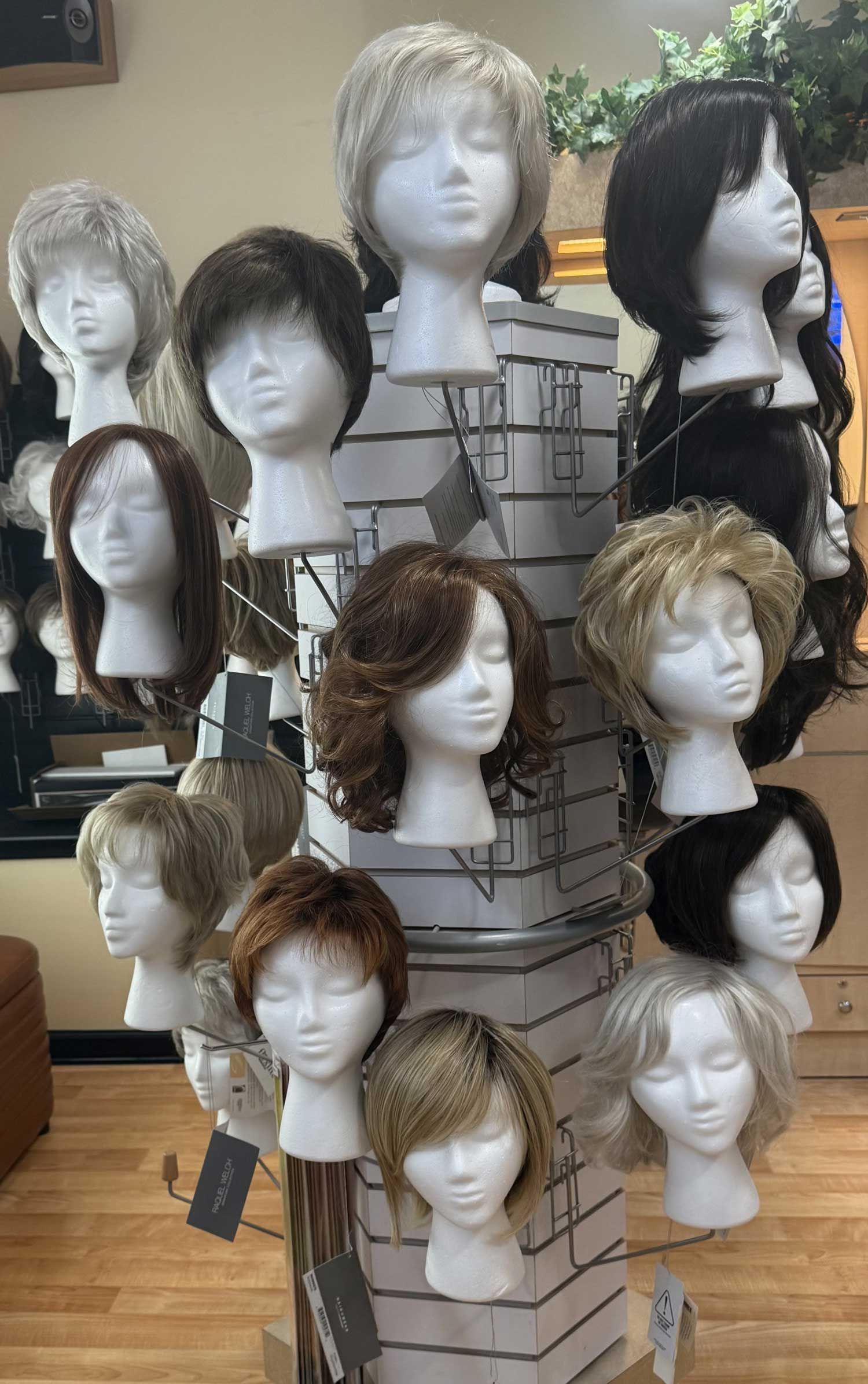 Display of mannequin heads wearing assorted wigs on shelves and stands in a store.