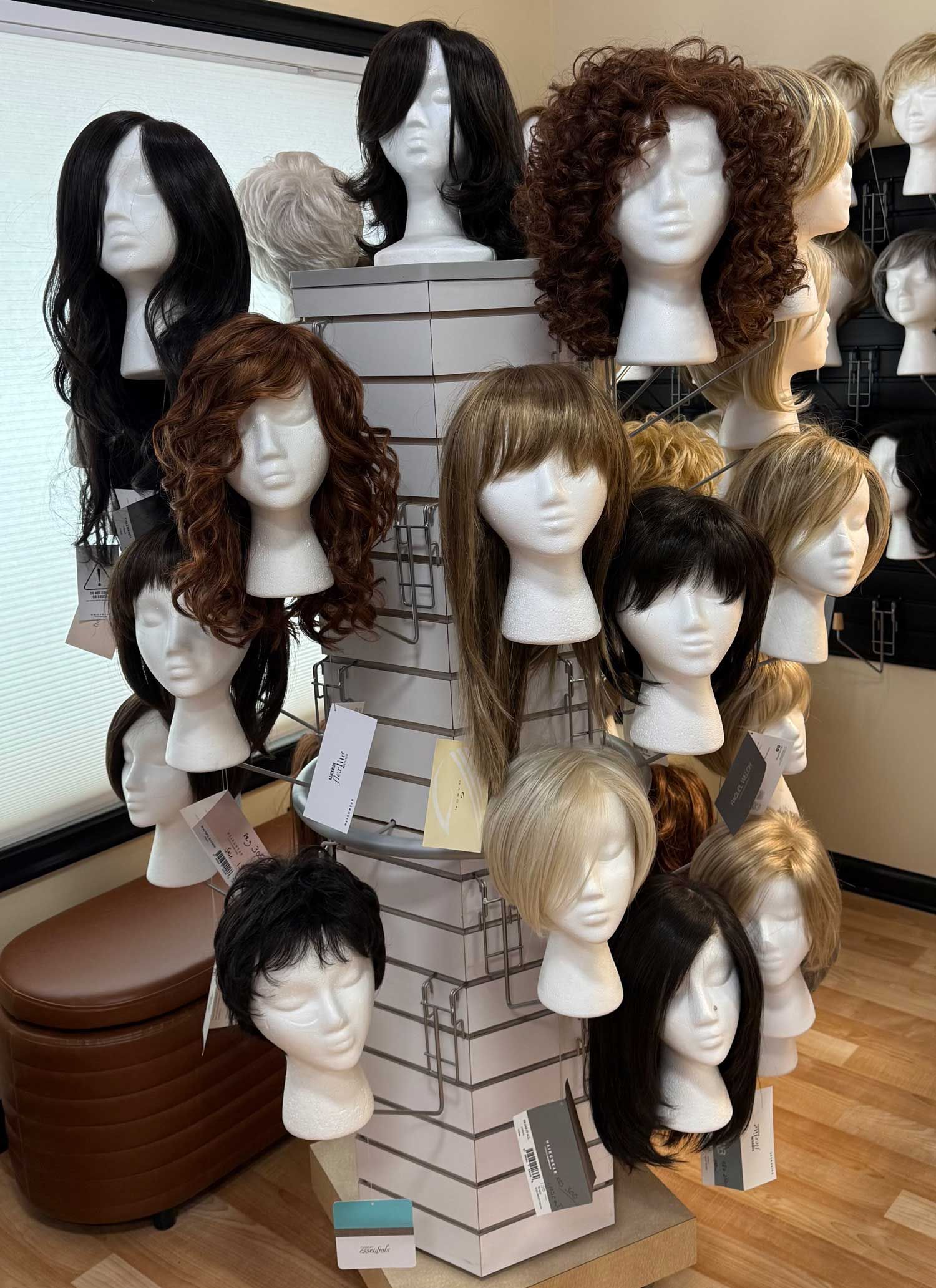 Display of mannequin heads with assorted wigs on rotating stands in a store or salon.