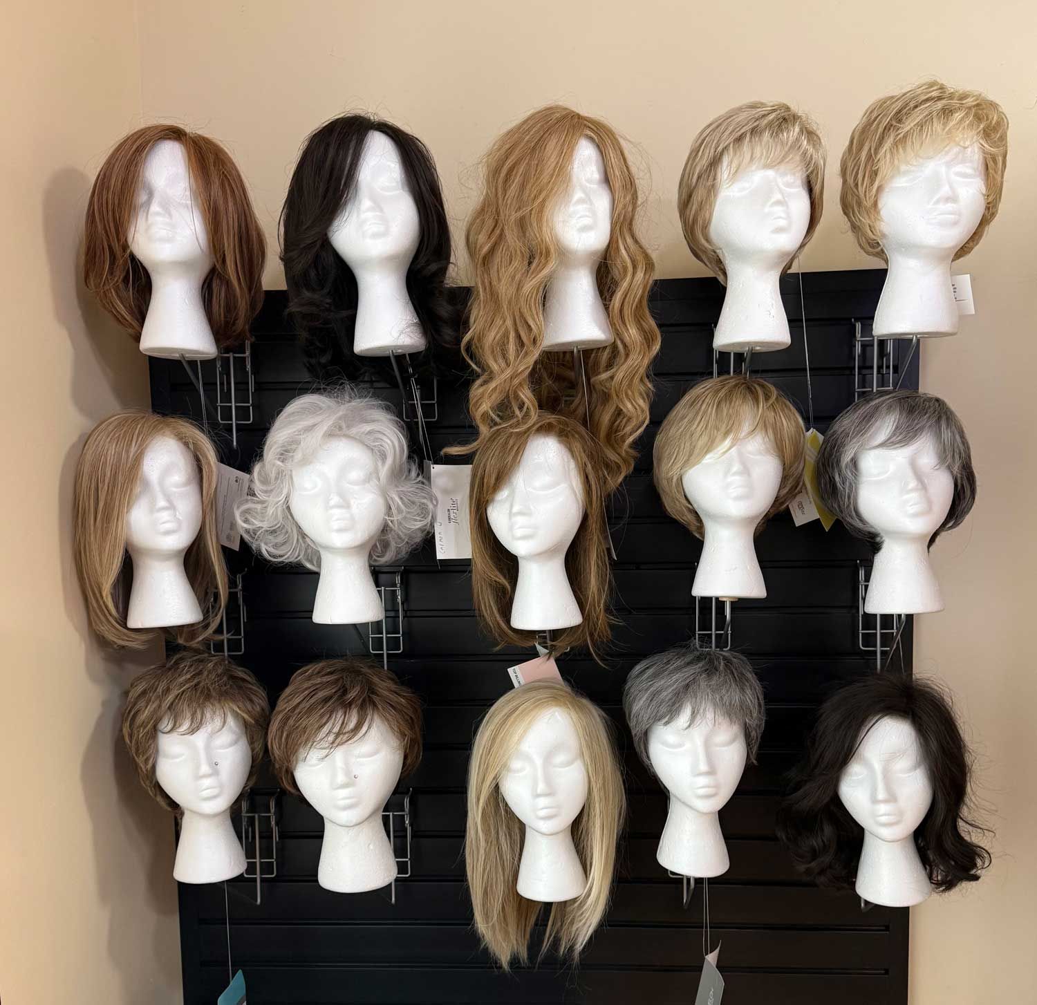 Assorted wigs on mannequin heads displayed on a wall rack in various colors and styles