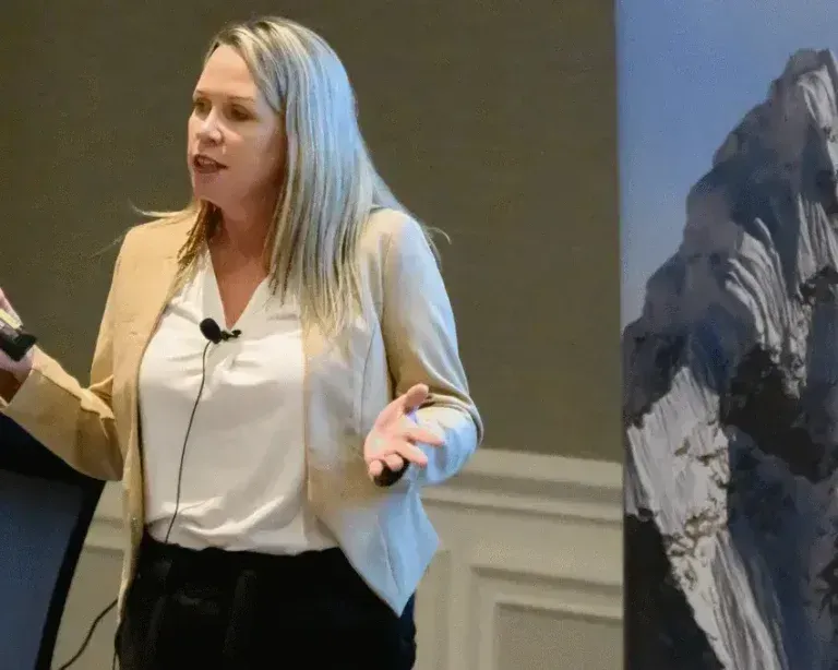 Speaker presenting on stage beside a mountain display banner