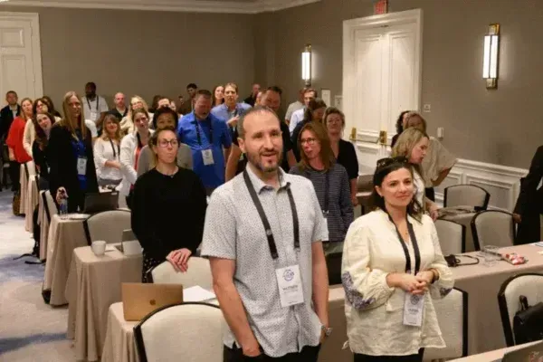 Conference attendees standing in a meeting room with tables and chairs