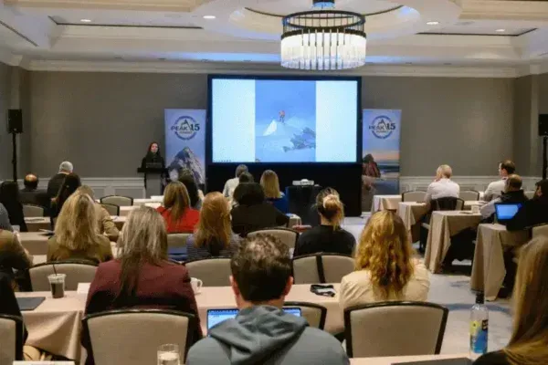 Conference attendees seated facing a large presentation screen in a hotel ballroom