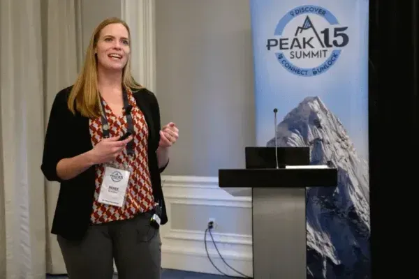Woman speaking at a podium beside a PEAK 15 Summit banner