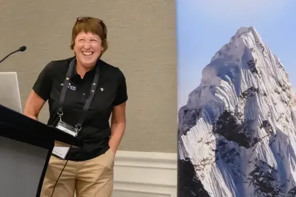 Woman smiling beside podium in conference room, with mountain image displayed on screen