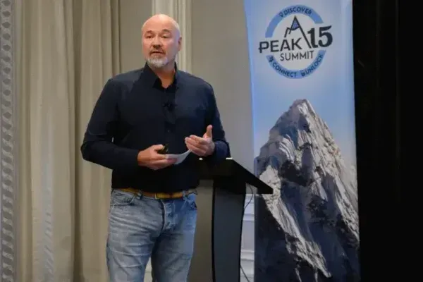 Speaker at a podium beside a Peak 15 Summit banner with a mountain graphic