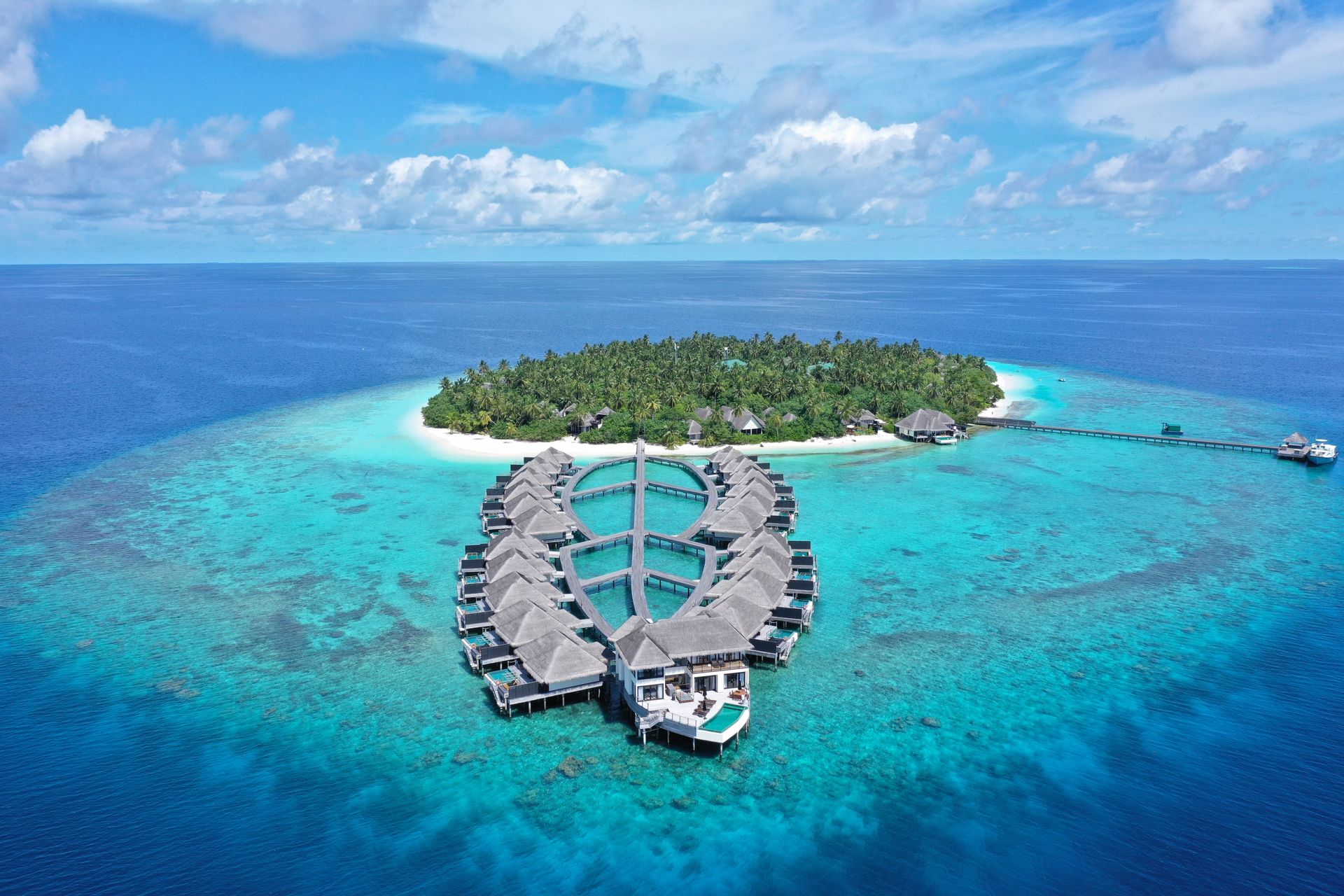 Aerial view of a tropical island resort with overwater villas in bright turquoise ocean