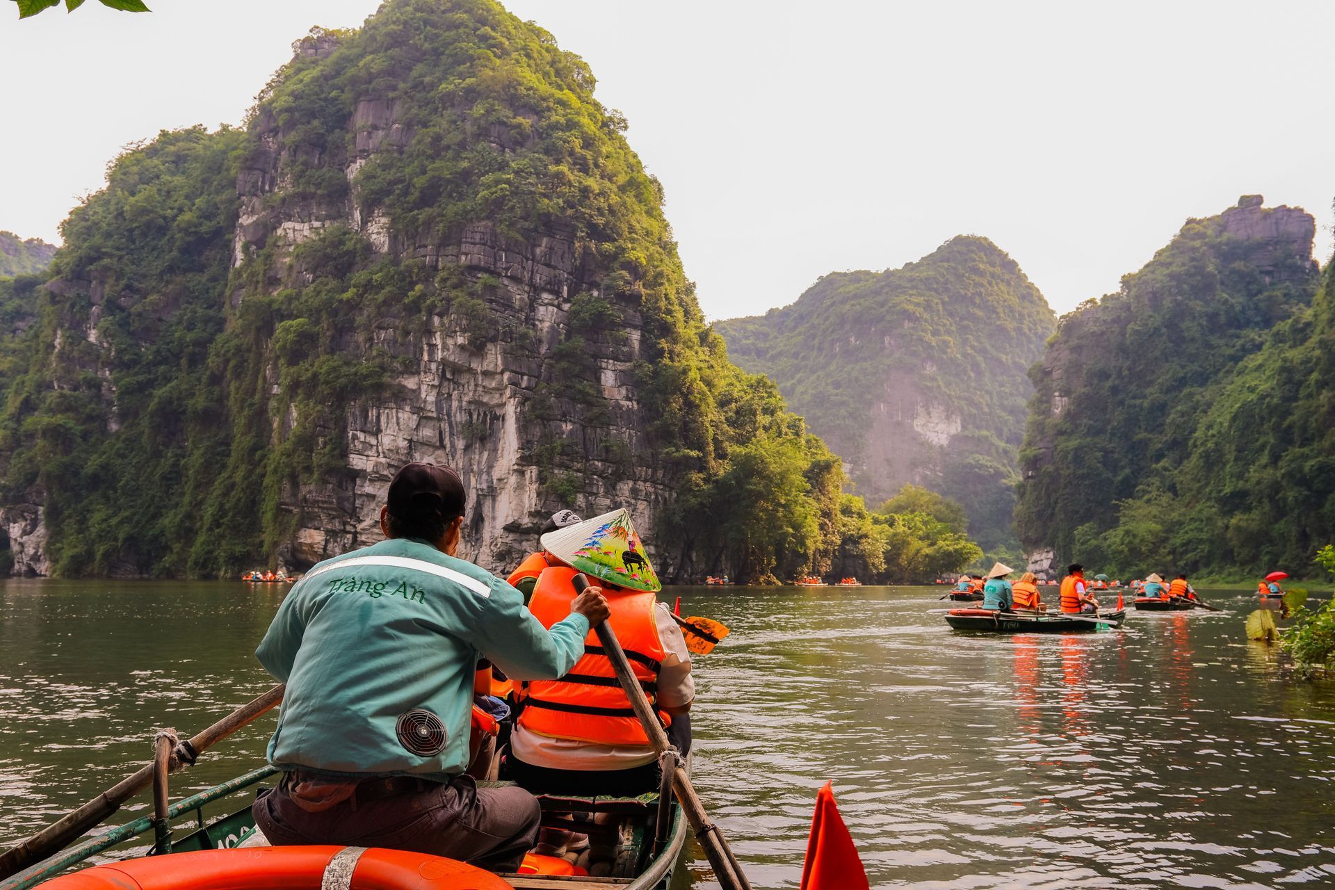 People in orange life jackets paddling kayaks on a river between steep green cliffs