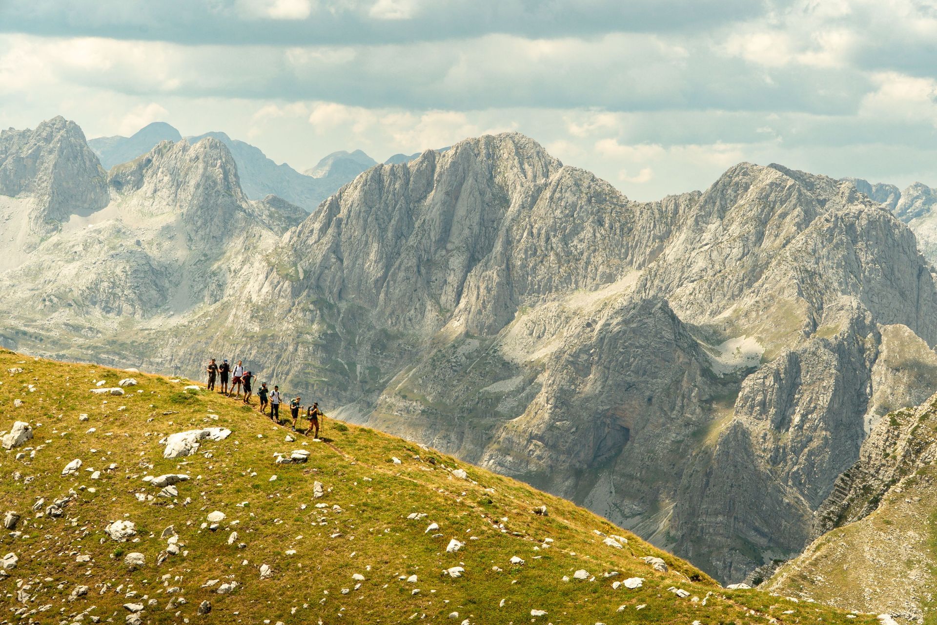 Hikers on a grassy mountain ridge with rugged gray peaks in the background