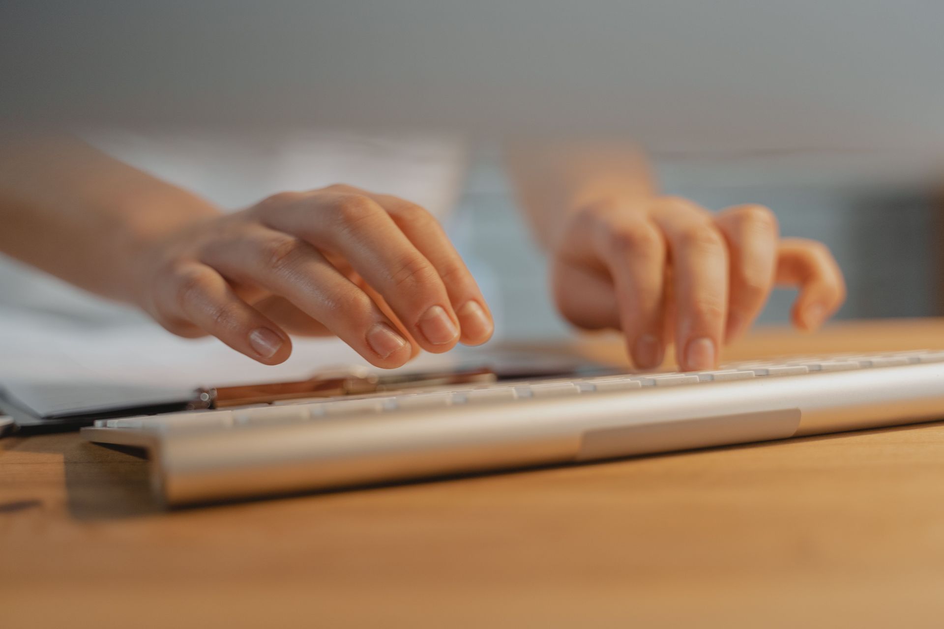 Hands typing on a laptop keyboard at a wooden desk