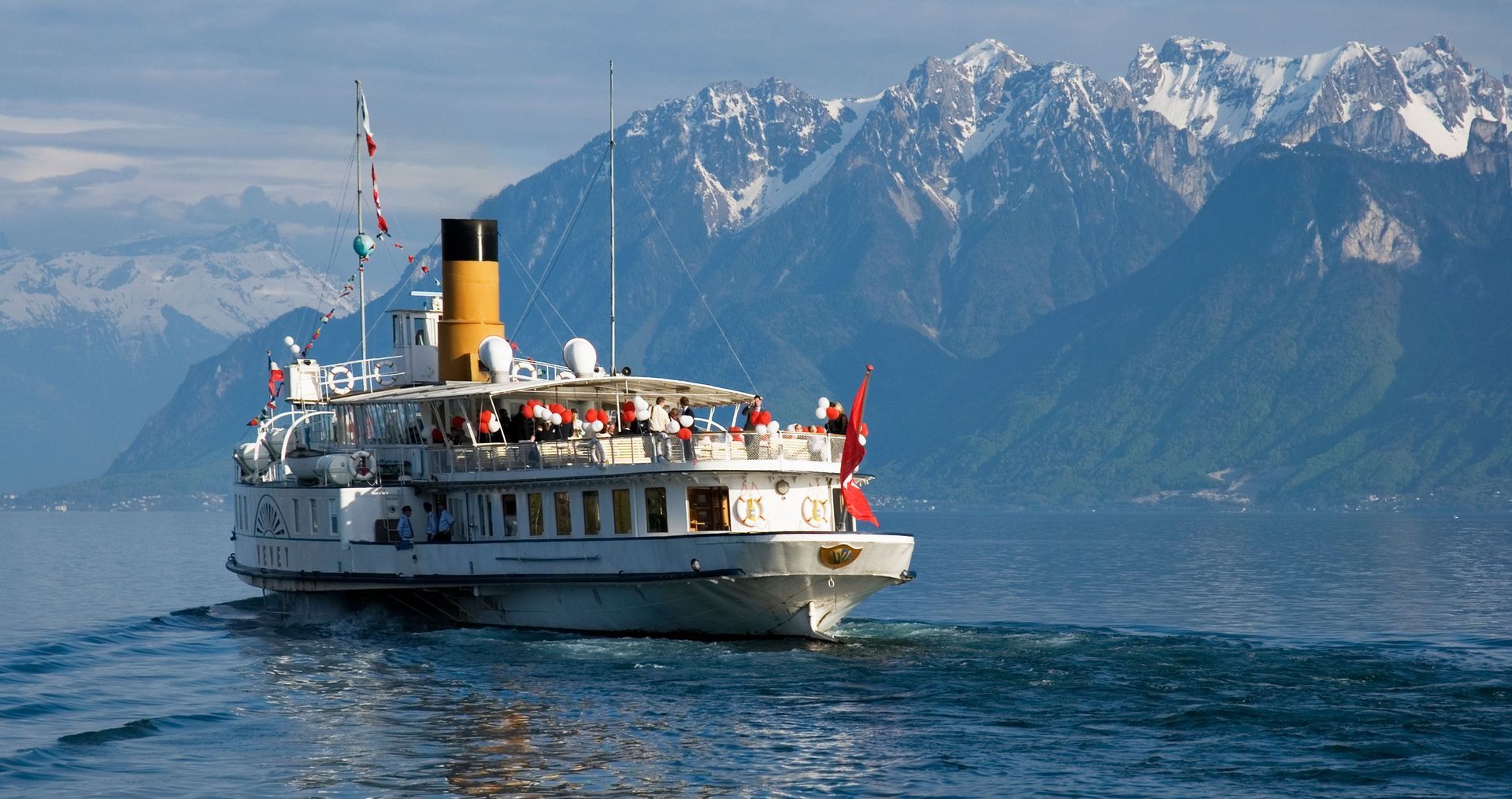 White ferry boat on blue water with snowy mountains in the background