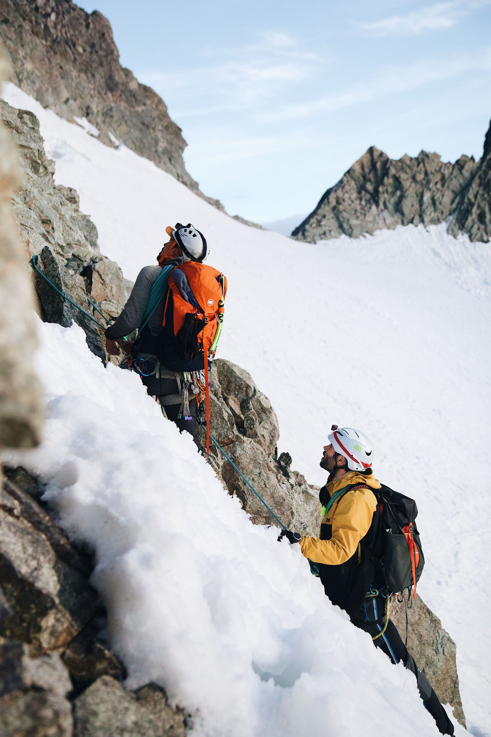 Two climbers in bright gear ascending a snowy mountain ridge