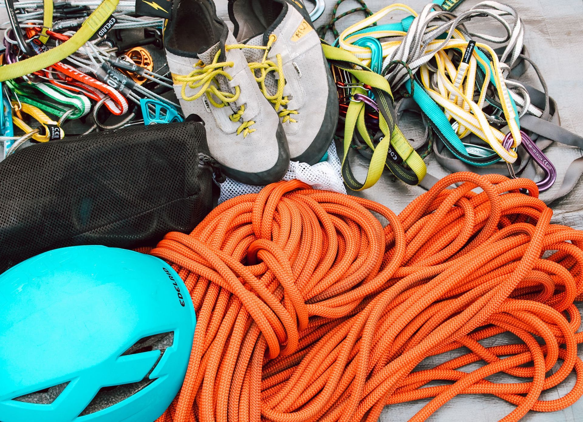 Climbing gear laid out: ropes, harnesses, helmets, shoes, and carabiners in bright colors.