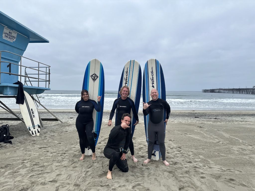 Four people posing on a beach with surfboards beside a blue lifeguard tower.