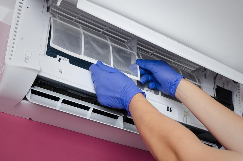 A Person Wearing Blue Gloves is Cleaning an Air Conditioner — Atmosphere Air Conditioning & Refrigeration In Medowie, NSW